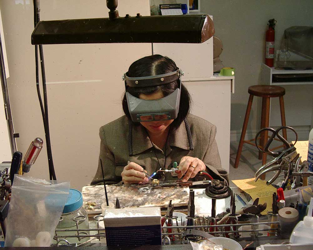 a women sits at a desk repairing jewellery